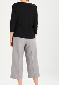 Schwarzes Dreiviertelarm-Oberteil mit rundem Halsausschnitt, kombiniert mit grau gesteppter, weiter Hosenhemmung aus einem weichen, strukturierten Stoff.
