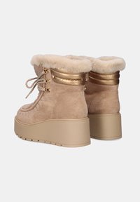 Botas de plataforma de ante beige con forro de piel de pelo, detalles en dorado y costuras decorativas. Presentan un diseño con cordones y suela de goma texturizada.