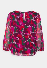Blouse transparente multicolore présentant un motif floral dans des nuances de rose, rouge et vert. Coupe ample avec manches longues et fermeture dos à œillet.