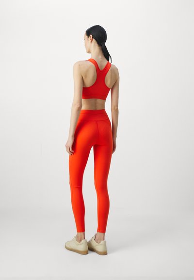 Red sports bra and matching high-waisted leggings made of stretchy material. The outfit features a racerback design and sleek, smooth texture.