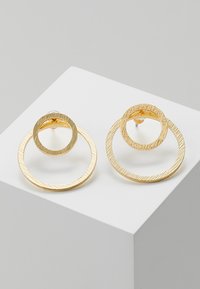 Ohrringe in Goldoptik, die aus zwei ineinandergreifenden Ringen bestehen – einem strukturierten und einem glatten – und ein minimalistisches Design auf einem hellen Hintergrund präsentieren.