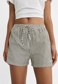 Krótkie spodenki w paski z sznurkiem w pasie, z naprzemiennymi jasnymi i ciemnymi pionowymi paskami, wykonane z lekkiego materiału.