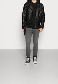 Czarna skórzana kurtka motocyklowa z srebrnymi elementami, szare dopasowane dżinsy i czarno-białe niskie sneakersy. Czarna bluza z kapturem pod kurtką.