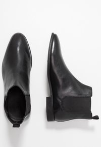 Ett par svarta läderanklar med elastiska sidopaneler och låga staplade klackar på en vit bakgrund.