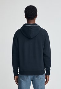 Felpa blu navy con cappuccio e maniche a raglan, realizzata in tessuto morbido. Presenta un orlo e polsini a coste, abbinati a jeans azzurri chiari.