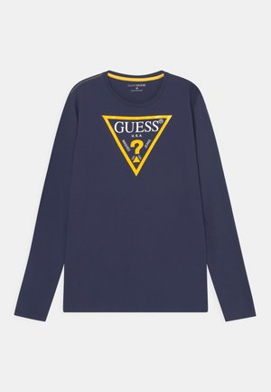 Navyblå langærmet skjorte med trekantet logo med gul kant og teksten "GUESS U.S.A." samt et gult spørgsmålstegn inde i trekanten.