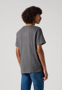 Grå bomulds T-shirt med korte ærmer, rund halsudskæring og en glat tekstur. Båret med blå jeans; set fra bagsiden.