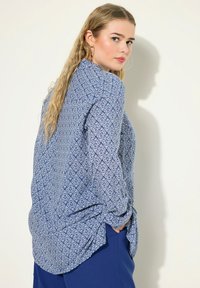 Blusa blu a fantasia con design geometrici bianchi, maniche lunghe e vestibilità morbida, con orlo arrotondato e polsini con bottone.