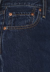 Tmavě modré džíny z denimu v detailu, s malou přední kapsou s měděnými nýty, kontrastním prošíváním a měkkou, texturovanou povrchovou úpravou.