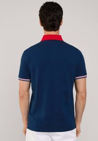 Marineblaues Poloshirt mit rotem Kragen. Die kurzen Ärmel verfügen über gerippte Akzente in Weiß und Rot. Einfaches, enganliegendes Design mit glatter Textur.