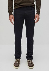 Mörkblå slim fit-jeans i bomullsblandning, ihop med bruna sneakers med vita sulor och snören, bära med en brun tröja.