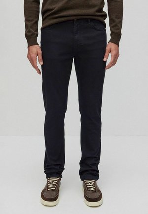 Mörkblå slim fit-jeans i bomullsblandning, ihop med bruna sneakers med vita sulor och snören, bära med en brun tröja.