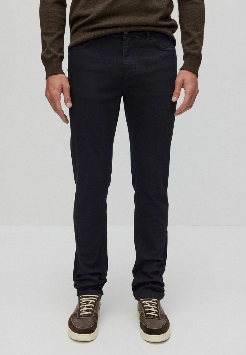 Mörkblå slim fit-jeans i bomullsblandning, ihop med bruna sneakers med vita sulor och snören, bära med en brun tröja.