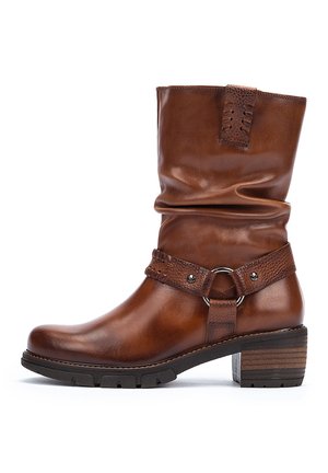 Brown leather ankle boot with slouchy shaft, textured leather strap, metal accents, and a chunky heel. Rubber outsole for support.