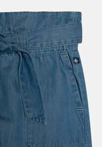 Denim kratke hlače svetlo modre barve, z napenjalnim pasom, elastičnim pasom in stranskimi žepi. Enostavna tekstura s kontrastnim šivom.