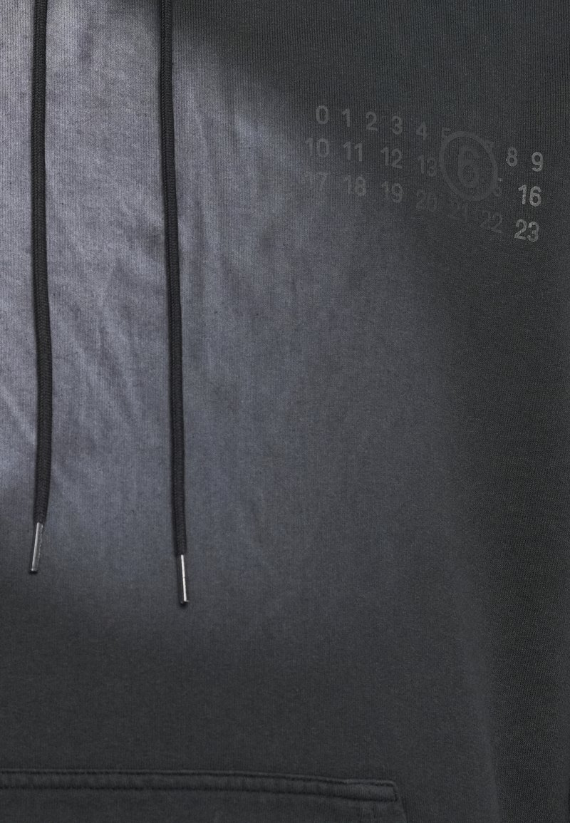 Schwarzer Hoodie mit glatter Textur, ausgestattet mit zwei Kordeln mit Metallspitzen und einem dezenten Druck von Zahlen an der Seite.