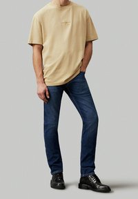 Beige bomull t-shirt med rund hals och liten broderad logotyp, i kombination med mörkblå denimjeans och svarta snörade stövlar.