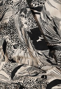 Tissu beige avec des motifs floraux abstraits noirs et des pois, comportant des plis et un détail de nœud torsadé.