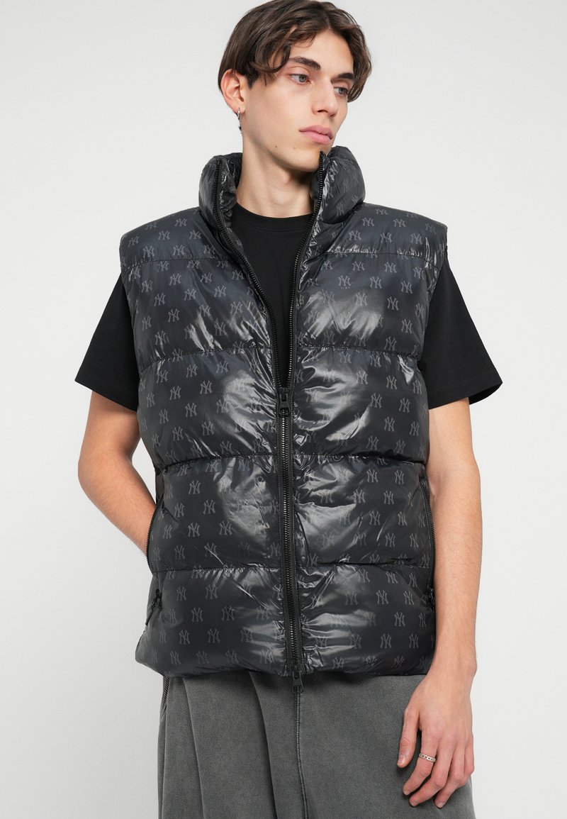 Black puffer vest with a high collar, featuring a repeating logo pattern. Smooth, shiny material with zip closure and side pockets.
