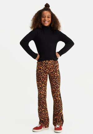Maglione a collo alto nero a coste, pantaloni a zampa d'elefante con stampa leopardata arancione e marrone e strisce nere sui lati, e sneakers rosse con lacci bianchi.