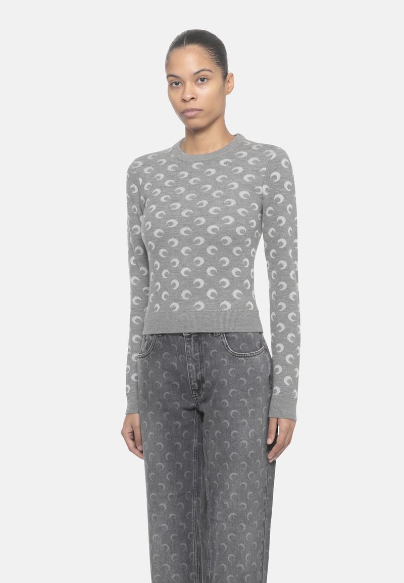 Maglione grigio a maglia con maniche lunghe, decorato con un motivo a luna crescente ripetuto in un grigio più chiaro sul corpo. Abbinato a jeans grigi con motivo.