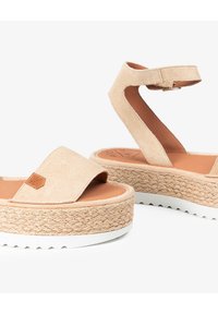 Sandalias de plataforma de ante beige con una media suela de yute trenzado, suela blanca y correa ajustable en el tobillo. Detalles texturizados en la parte superior.