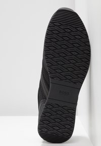 Semelle de chaussure de sport noire avec une surface en caoutchouc texturé présentant un motif en losange et le logo "HUGO BOSS" en relief. Design simple sans accents.