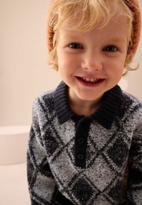 Jersey de punto con un patrón de rombos en tonos de gris y negro, con un cuello acanalado oscuro y una tapeta con tres botones.