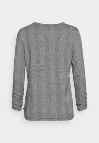 Blusa de manga larga de cuadros que presenta un patrón geométrico en blanco y negro, con cuello redondo y una tela ligeramente texturizada.