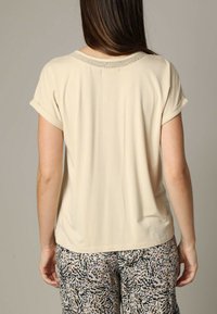 T-shirt beige à manches courtes avec un col texturé, en tissu lisse et à coupe décontractée. Associé à un pantalon à motifs avec des éclats de couleurs.