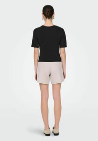 Camiseta negra de manga corta con escote redondo, combinada con pantalones cortos beige. La tela parece suave y ligera.
