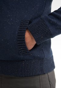 Gebreide marineblauwe trui met een gespikkelde textuur, voorzien van geribbelde manchetten en zoom, en een zijzak die in het ontwerp is geïntegreerd.