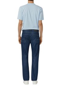 Hellblaues Kurzarmhemd kombiniert mit dunkelblauer Jeans, die zwei Gesäßtaschen hat, und weißen Turnschuhen, von hinten betrachtet.