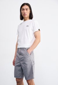 Camiseta blanca de algodón con un pequeño logo negro, combinada con pantalones cortos de carga grises claros hasta la rodilla que cuentan con bolsillos laterales y una textura suave.