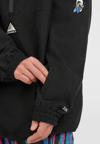 Zwarte waterdichte jas met elastische manchetten en een hand in een zijzak. Bevat een logo en een "20K" detail op de manchette.