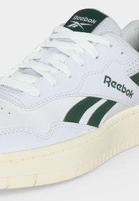Λευκό αθλητικό παπούτσι Reebok με σκουροπράσινες ρίγες, λευκά κορδόνια, υφασμένο πέλμα και λογότυπο Reebok στο πλάι και στη γλώσσα.