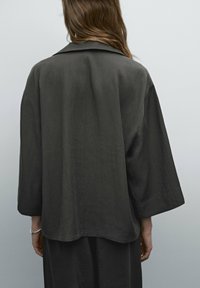 Chemise ample gris foncé avec un large col et des manches longues, présentant une texture douce et un design simple.