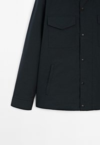 Giacca blu scuro realizzata in tessuto liscio, con colletto, due tasche a patta, una tasca laterale e chiusura a bottoni a pressione.