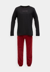 Čierna košeľa s dlhým rukávom s logom "Calvin Klein", skombinovaná s červenými pyžamovými nohavicami s jemným vzorom malých oranžových hviezd.