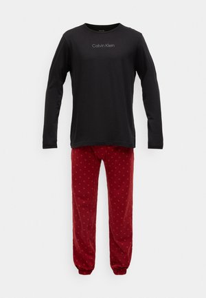 Camisa de manga longa preta com o logótipo "Calvin Klein", combinada com calças de pijama vermelhas com um padrão subtil de pequenas estrelas laranjas.