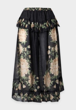 Femme portant un haut noir ajusté avec un détail fleur et une large jupe noire transparente à motif floral avec des volants et des chaussures plates beiges.