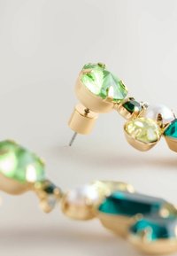 Goldene Ohrringe mit grünen und tealfarbenen Edelsteinen in facettierter Schnittform. Mit einem Perlenakzent und einer Sicherheitsnadel für einen sicheren Halt.