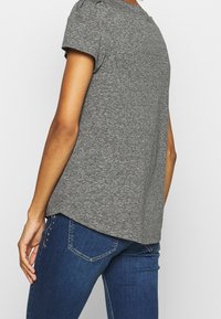 Grå kortærmet t-shirt med en afslappet pasform, blød tekstur og en buet kant, parret med mørkeblå jeans med subtile udsmykninger.