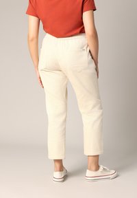 Crème-kleurige corduroy broek met een subtiele ribbeltextuur, voorzien van achterzakken en een relaxed fit, gecombineerd met witte sneakers.