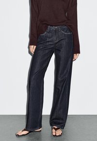 Dunkelblaue weite Jeans aus Denim, mit classic fünf Taschen-Design, Reißverschluss und Knopfverschluss.