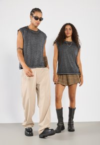 Two models display fashion items: a dark gray sleeveless top, beige wide-leg pants, a plaid skirt, and black ankle boots with hardware accents.