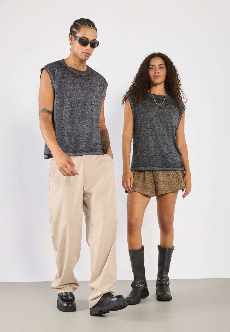 Two models display fashion items: a dark gray sleeveless top, beige wide-leg pants, a plaid skirt, and black ankle boots with hardware accents.