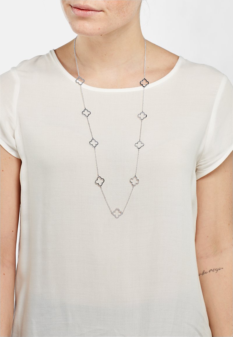 Collier en argent composé de formes florales entrelacées, alternant avec des accents transparents, présenté sur un haut clair.
