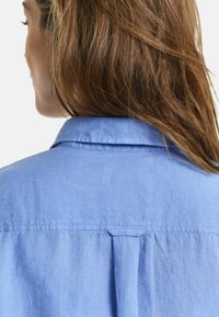 Lichtblauw shirt met een traditionele kraag, geplooide rugontwerp en een gestructureerde stof voor een zachte, ademende feel.