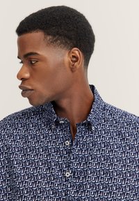 Navy Bluse mit aufgedrucktem weißen Segelboot-Muster, mit Kragen und Knopfleiste. Der Stoff wirkt glatt und leicht.